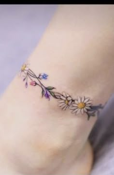 a woman's foot with daisies and leaves tattoo on the side of her leg