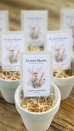 small white bowls filled with flowers on top of a wooden table next to cards that say let love bloom