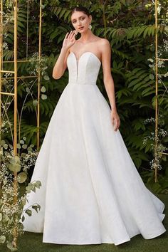 a woman in a white wedding dress standing next to a gold trellis and greenery