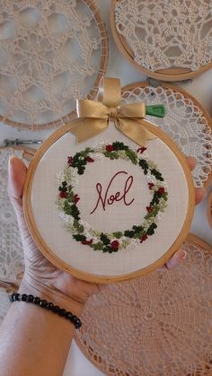 a person holding up a cross stitch christmas wreath with the word noel on it in front of some doily