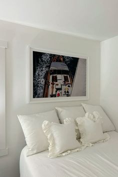 a white bed topped with pillows next to a framed photo on the wall above it