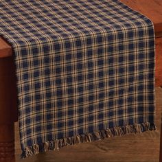 a plaid table runner with tassels on a wooden table in front of a window