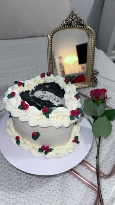 a white cake sitting on top of a table next to a mirror and a rose