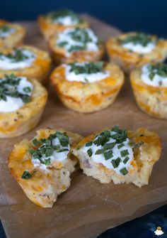 several mini quiches with cheese and herbs on top are sitting on wax paper, ready to be eaten