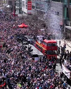 a large group of people standing on the side of a road next to a red double decker bus