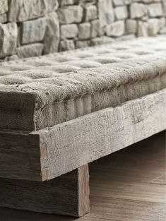 a bench made out of wood sitting on top of a hard wood floor next to a stone wall