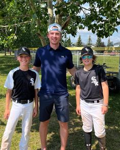 three young baseball players standing next to each other in front of a tree and fence