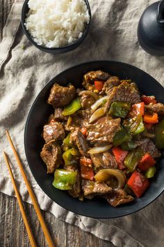 beef and peppers stir fry in a black bowl with chopsticks next to it