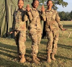 three women in camouflage uniforms standing next to a green tent and waving at the camera