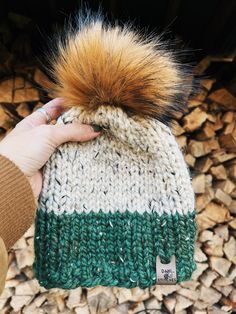 a person holding onto a knitted hat with a fur pom