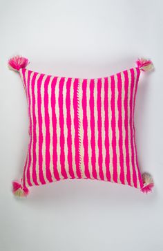 a pink and white striped pillow with tassels on the edges, sitting against a white wall