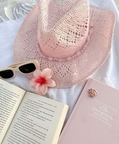 a pink hat, sunglasses and book on a white bed with a lace doily