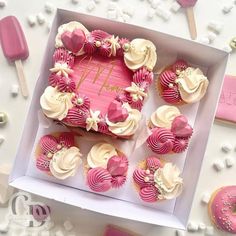 a box filled with pink cupcakes on top of a white table next to candy