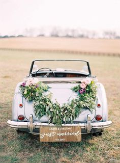 an old car decorated with flowers and greenery sits in the middle of a field