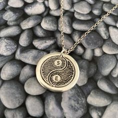 a silver necklace with the letter e on it sitting on some rocks and pebbles in black and white