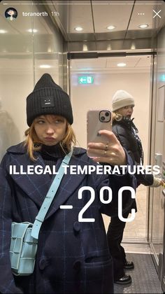 a woman taking a selfie in front of a mirror wearing a hat and coat