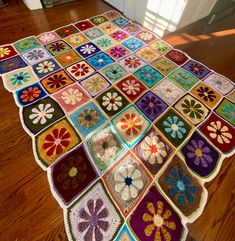 a multicolored crocheted rug on the floor with flowers and leaves in squares