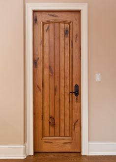 an image of a wooden door in a room that is painted white and has brown trim