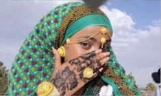 a woman with tattoos on her face and hands covering her eyes while wearing a green headdress