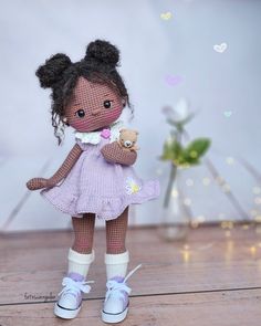 a small doll is holding a teddy bear in her hands and standing on the floor