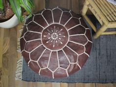 a brown and white ottoman sitting on top of a wooden floor next to a potted plant