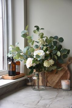 a vase filled with white flowers sitting on top of a counter next to a window