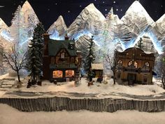 a christmas scene with snow covered mountains and houses in the foreground, surrounded by fake trees