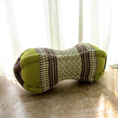 a green pillow sitting on top of a wooden table next to a window with white curtains