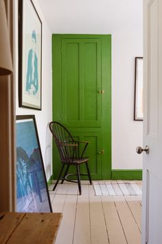 a green door in a white room with a wooden chair and framed pictures on the wall