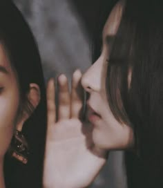 two young women are looking at each other's eyes with their hands on their faces