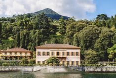 a large house sitting on top of a lush green hillside next to a body of water