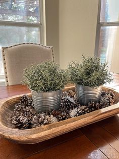 two tin cans filled with pine cones sitting on top of a wooden table next to a window