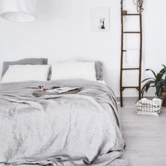 an unmade bed in a white room with grey linens and pillows on it