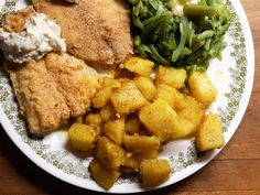 a white plate topped with meat, potatoes and green veggies on top of a wooden table