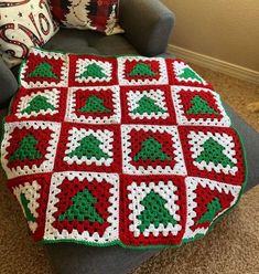 a crocheted christmas blanket sitting on top of a chair next to a pillow