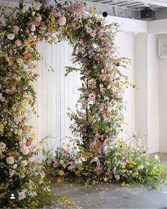 an arch covered in flowers and greenery next to a white wall on the floor