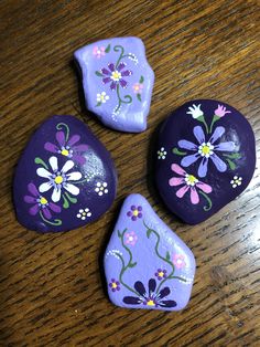 three painted rocks with flowers on them sitting on a wooden table next to each other