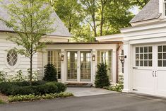 a white house with trees and bushes in front of the garage door is surrounded by greenery