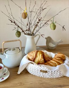 croissants in a basket on a table next to a teapot and cup