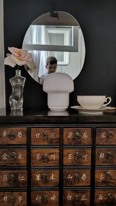 a dresser with a mirror, bowl and vase on it in front of a man's reflection