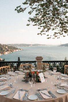 an outdoor table set with place settings for dinner overlooking the ocean and town below it