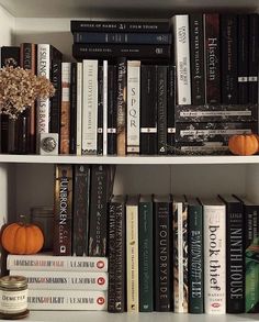 a book shelf filled with lots of books next to a vase and some pumpkins