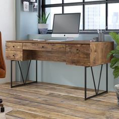 an office desk with a computer on it in front of a window and potted plant