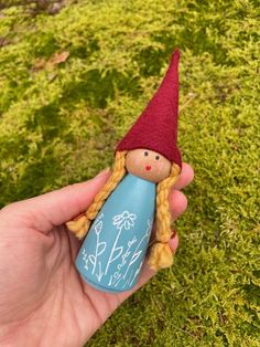 a hand holding a small doll in the grass