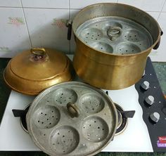 two pots sitting on top of a stove next to an open frying pan with holes in it