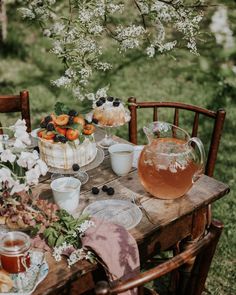 a wooden table topped with plates and bowls filled with fruit next to flowers on top of a lush green field