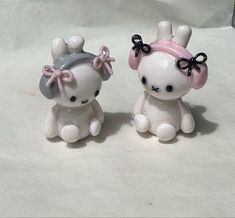 two white ceramic figurines with black bows on their heads and ears sitting next to each other