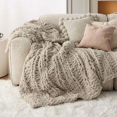 a couch covered in blankets and pillows on top of a white rug