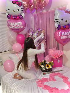 a woman sitting on top of a bed with pink balloons and hello kitty birthday decorations