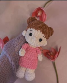 a crocheted doll with a pink shirt and brown hair is sitting next to flowers